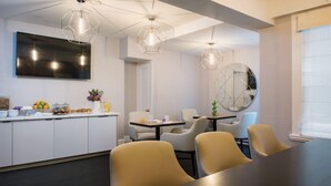 A modern dining area with a long table and chairs, a kitchen counter with breakfast items, and geometric pendant lighting. - Inn At Union Square (San Francisco)