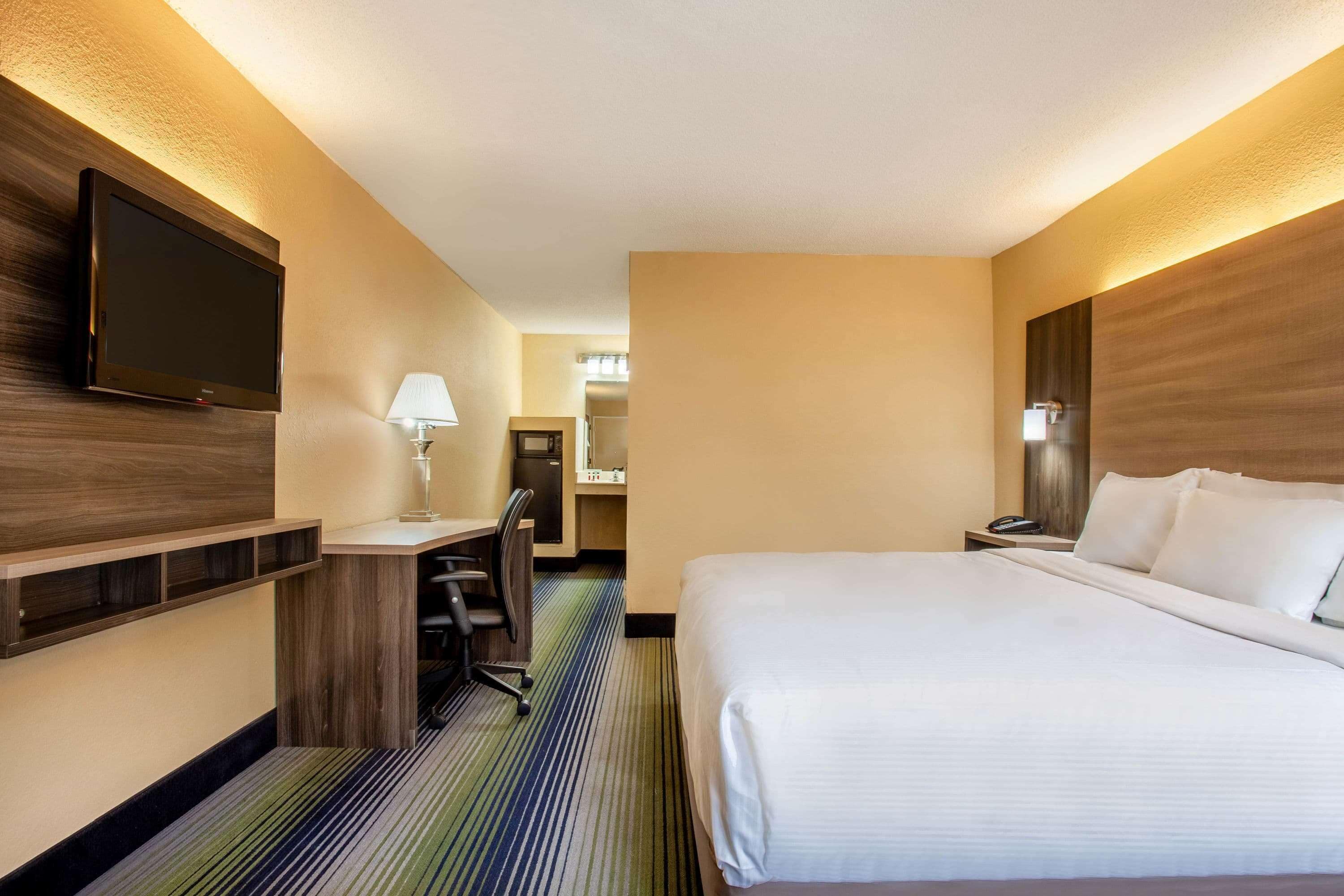 A hotel room with a bed, desk, chair, TV, and a mirror.