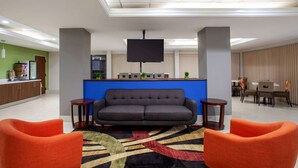 Un vestíbulo moderno con un sofá, dos sillones, un televisor de pantalla plana, una recepción y una zona de comedor.