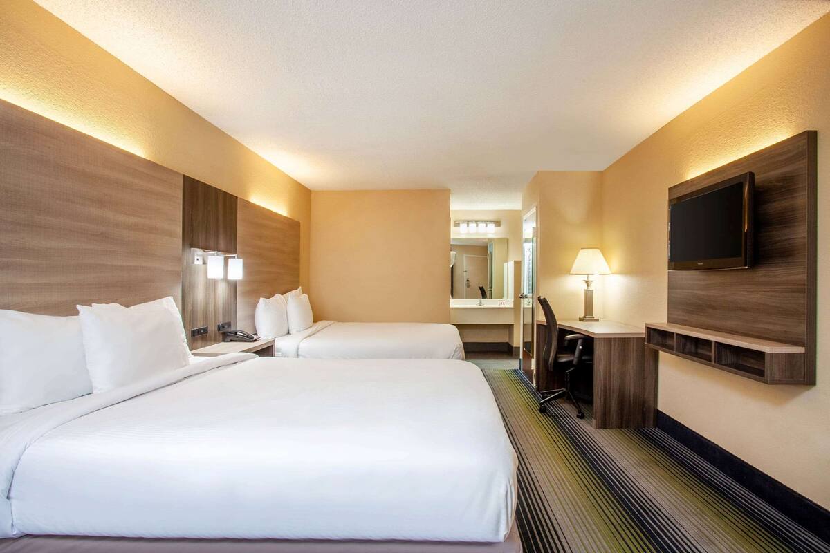 Ein Hotelzimmer mit zwei Betten, einem Schreibtisch, einem Stuhl, einem Fernseher und einem Spiegel.