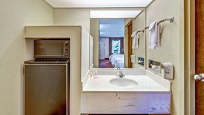 Un baño de hotel pequeño con lavamanos, espejo, toallero y microondas.