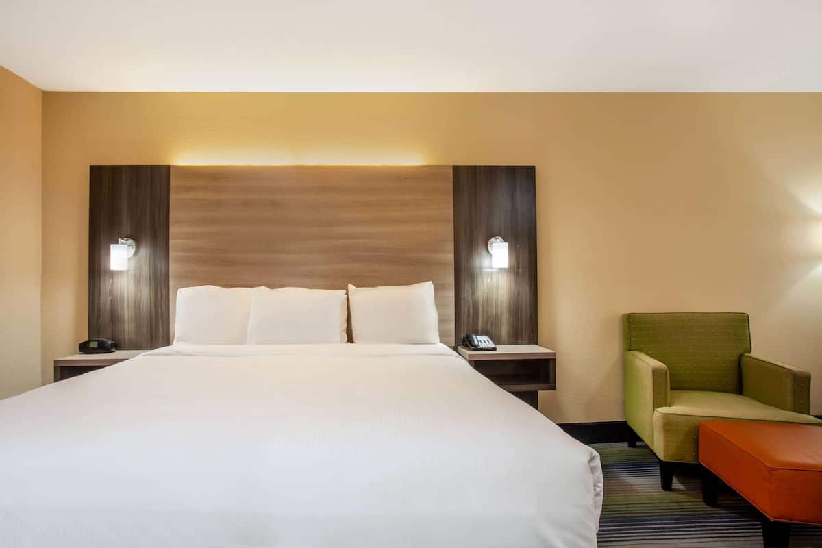 Ein Hotelzimmer mit einem großen Bett, zwei Nachttischen mit Lampen, einem grünen Sessel und einem kleinen orangefarbenen Hocker.