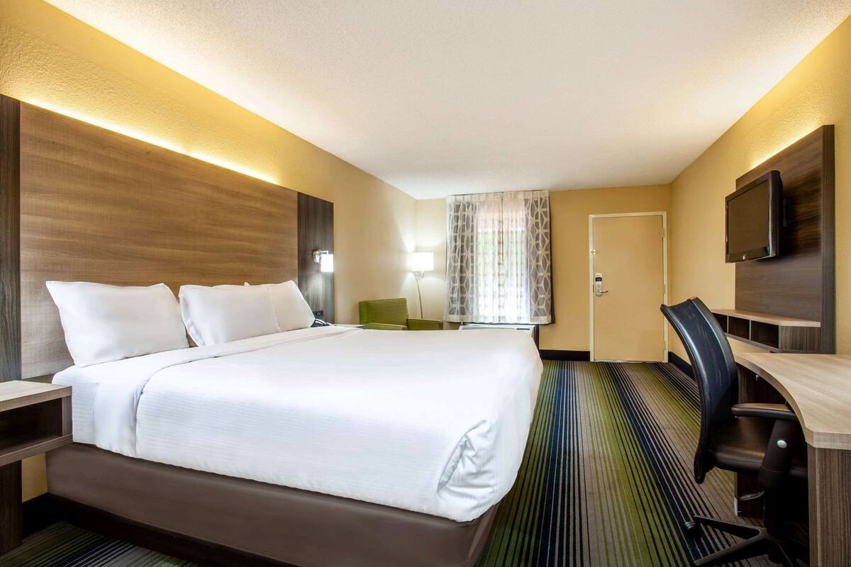 Ein Hotelzimmer mit einem großen Bett, einem Schreibtisch, einem Stuhl, einem Fernseher und einer Lampe.