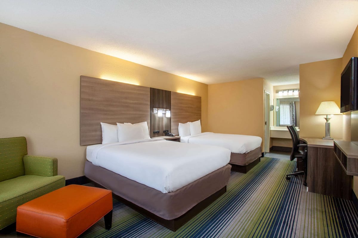 Ein Hotelzimmer mit zwei Betten, einem Schreibtisch, einem Sessel, einer Couch und einem Fernseher.