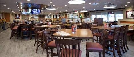 Um restaurante espaçoso com várias mesas e cadeiras, um balcão e uma televisão exibindo esportes.