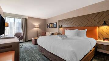 A hotel room with a large bed, a desk, a chair, and a television.
