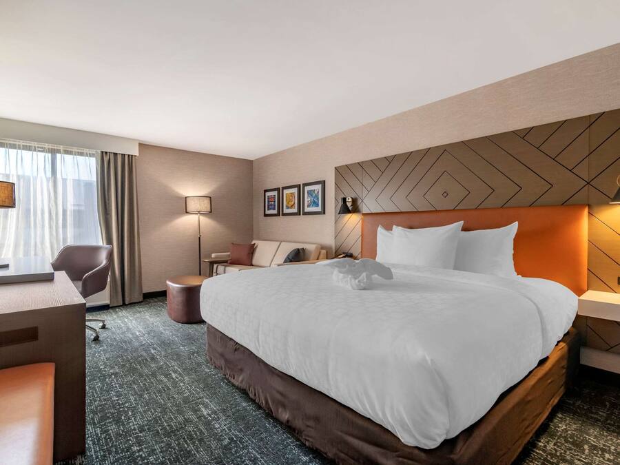 A hotel room with a large bed, a desk, a chair, and a television.