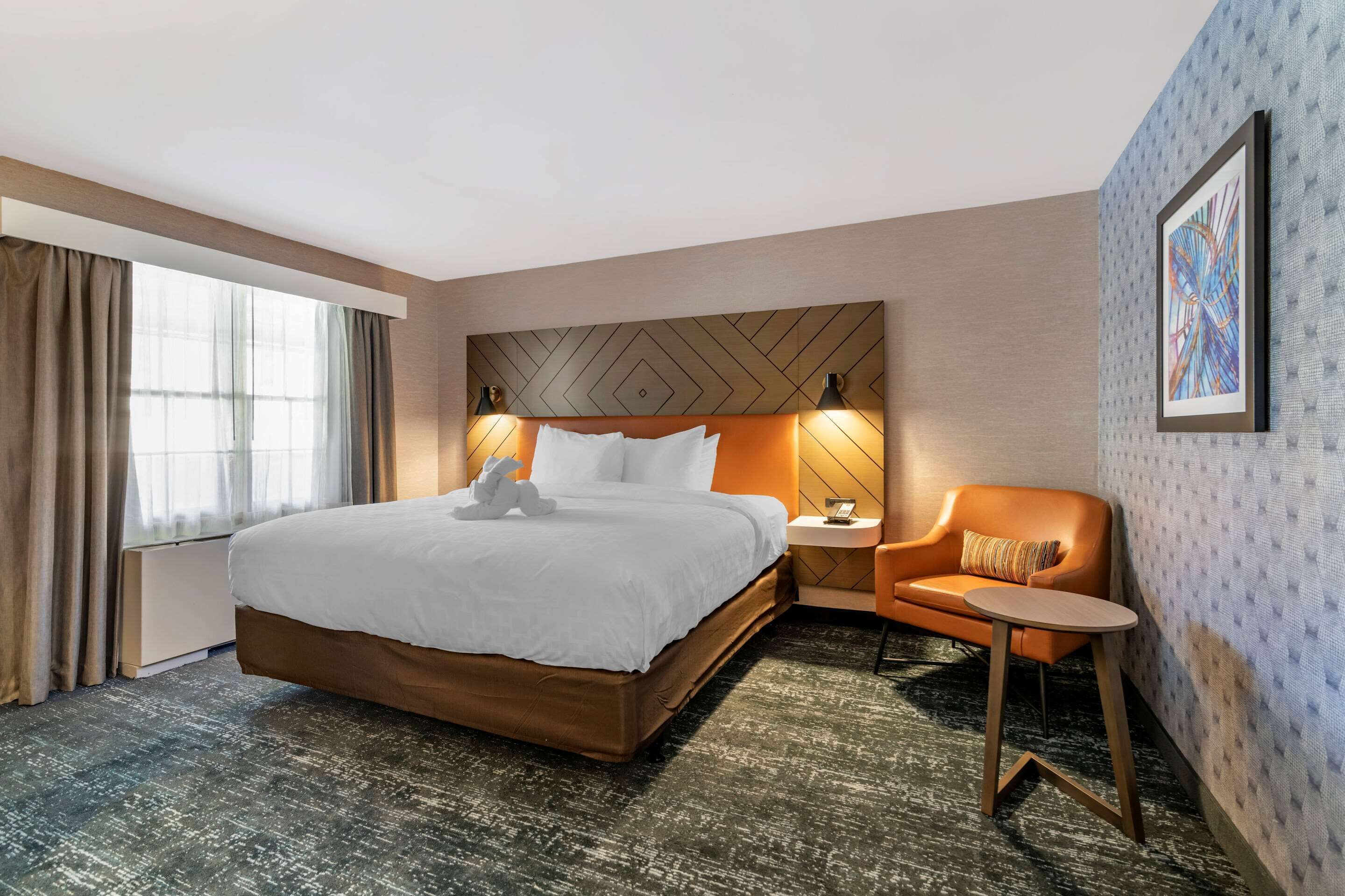 A hotel room with a large bed, a nightstand, a chair, and a window with curtains.