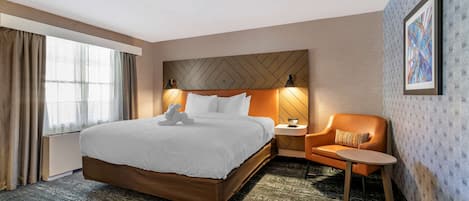 A hotel room with a large bed, a nightstand, a chair, and a window with curtains.