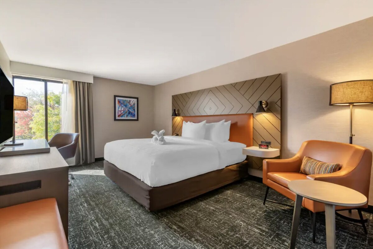 Una habitación de hotel con una cama grande, un escritorio, una silla, una mesita y un televisor.