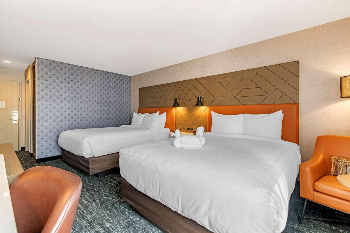 Habitación de hotel con dos camas, un sofá, una silla y un cabecero decorativo.