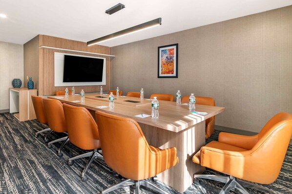 A conference room with a large table, orange chairs, a flat-screen TV, and a water dispenser.