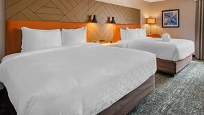 A hotel room with two beds, a geometric-patterned headboard, wall-mounted lamps, and a framed abstract painting. - Clarion Inn Nashua (Nashua)