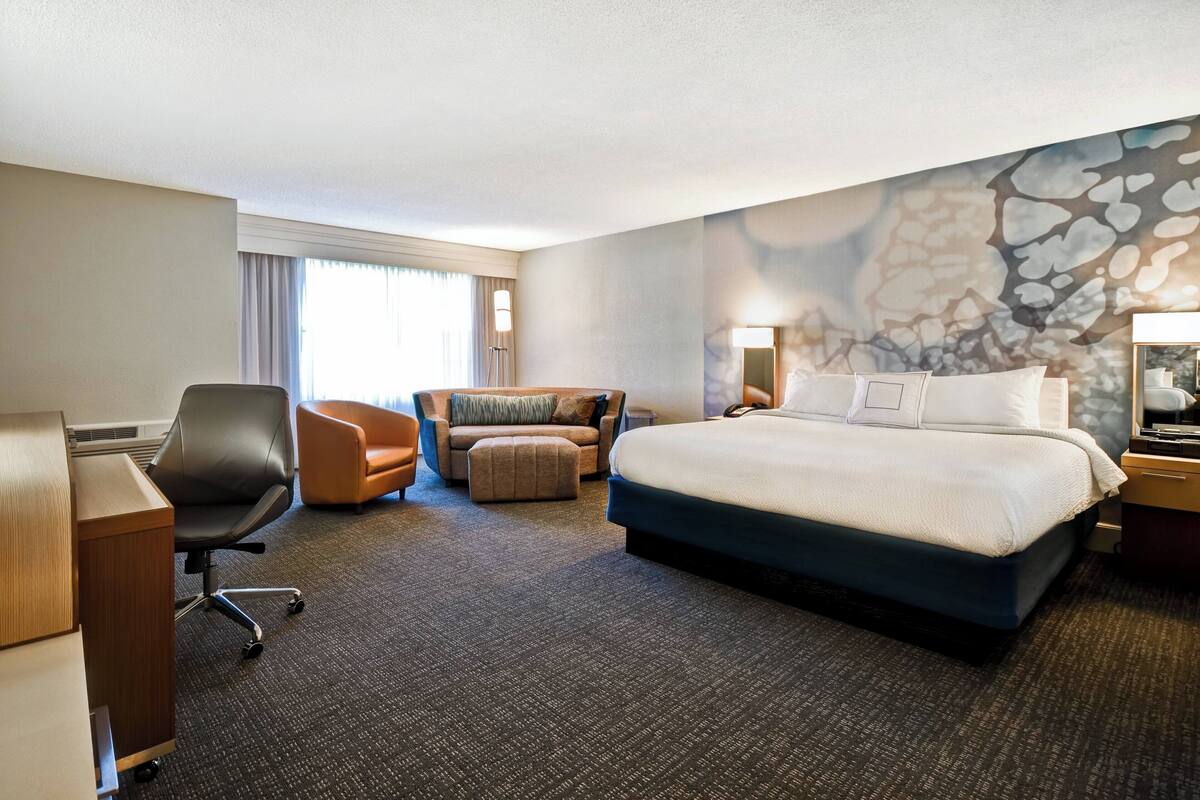 A hotel room with a large bed, a desk, an office chair, a sofa, and a carpeted floor.