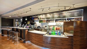 Zona de bar moderna con una barra curva de madera, varios taburetes y una vitrina con bebidas.