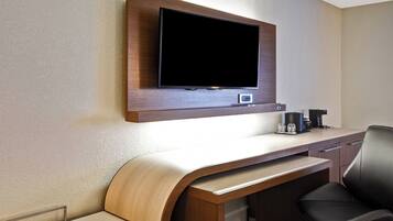 Een hotelkamer met een flatscreen televisie aan de muur, een houten bureau met een gebogen voorkant, een zwarte lederen fauteuil en een koffiezetapparaat op het bureau.