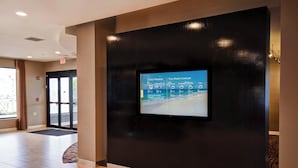Zona de recepción de hotel con una pantalla digital que muestra el clima actual y la previsión semanal.