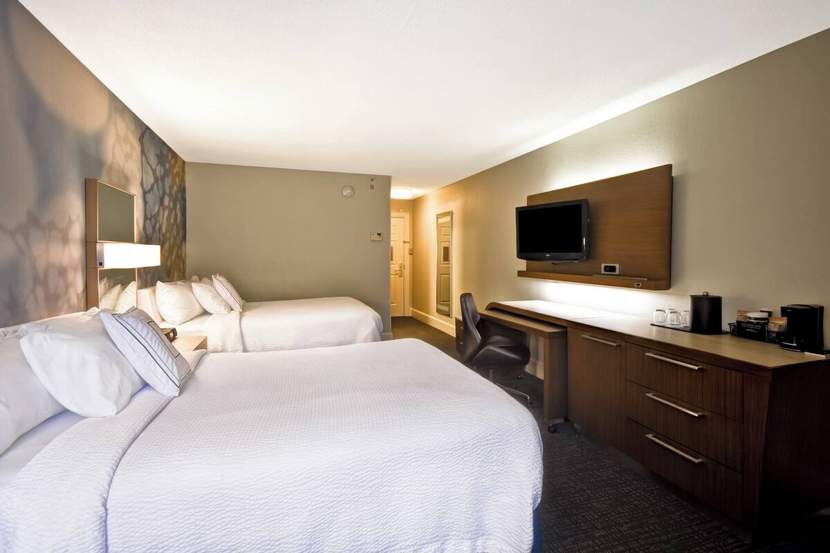 A hotel room with two beds, a desk, a chair, a TV, and a coffee maker.