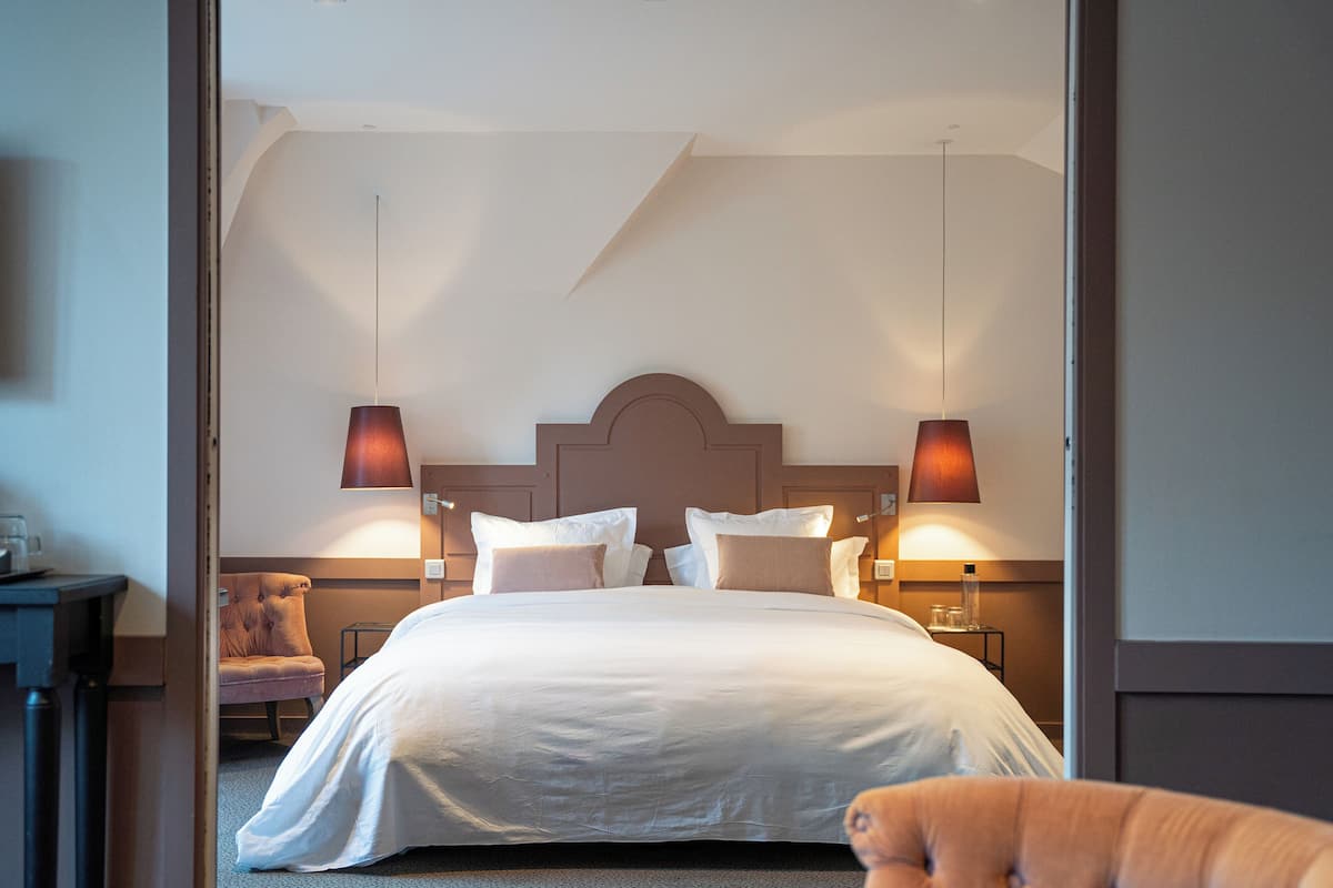 A hotel room with a large bed, two bedside lamps, a chair, and a nightstand.