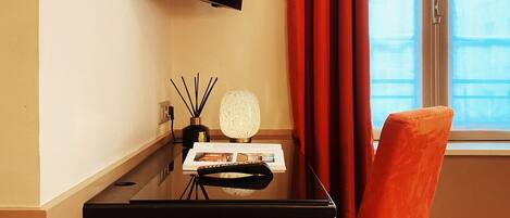 Een hotelkamer met een flatscreen televisie aan de muur, een houten bureau met een afstandsbediening, een tijdschrift en een decoratieve lamp.
