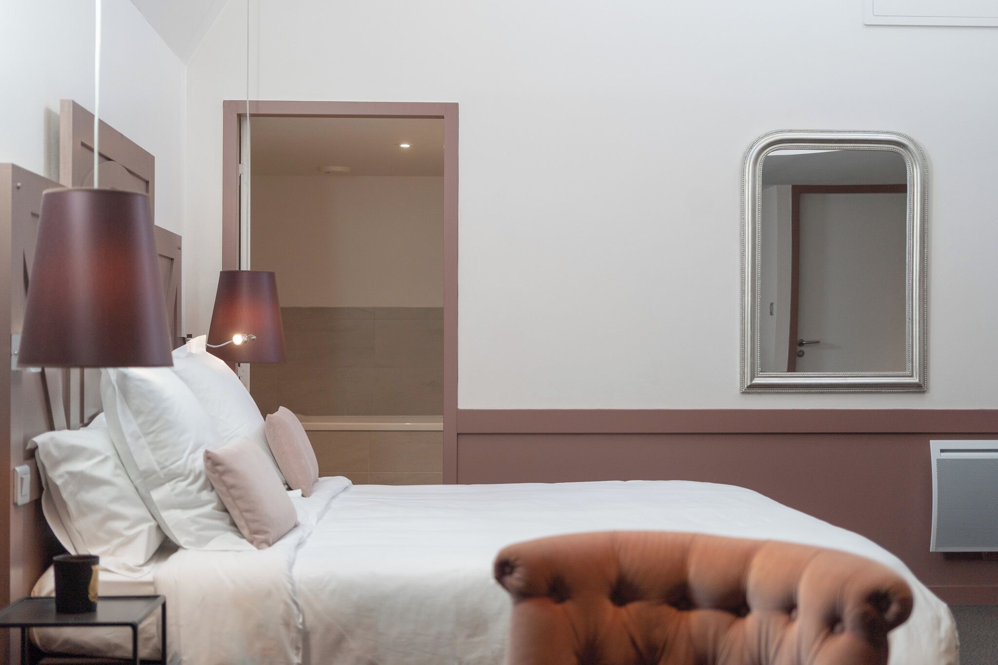 A neatly made bed with white linens, a bedside lamp, and a chair.