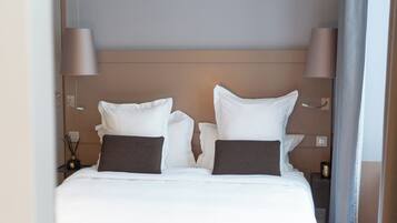 A hotel room with a bed, two bedside lamps, a nightstand, and a wall-mounted outlet.