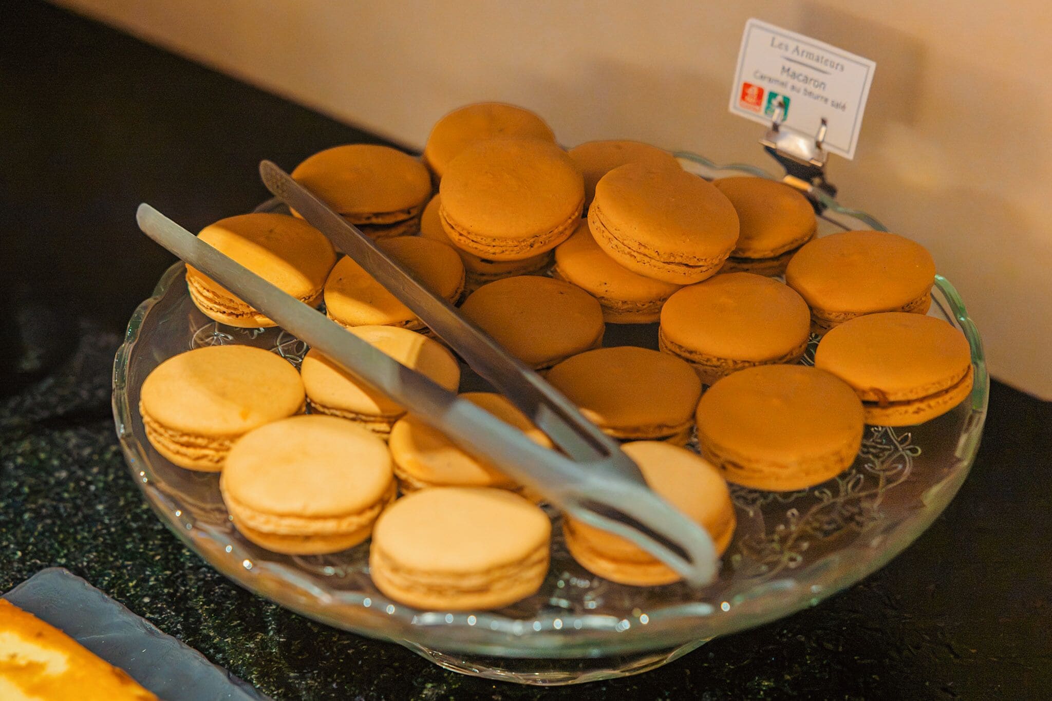 En glasskiva med macarons och en skylt som visar ”Les Armailloirs” och ”Macaron”.