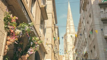 A narrow street with historic buildings, a classic car, and colorful flags.