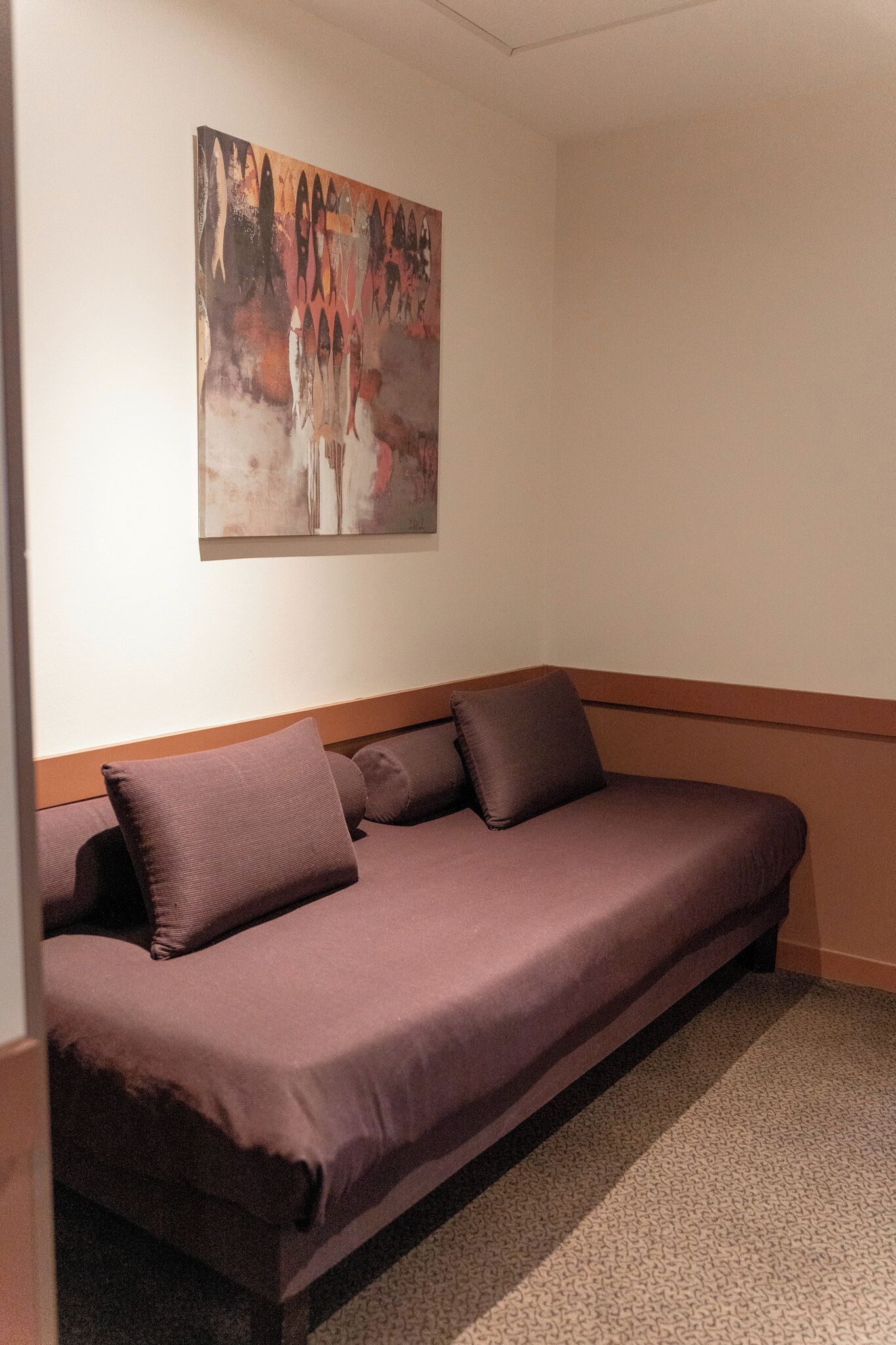 A room with a single bed, a painting on the wall, and a wooden headboard.