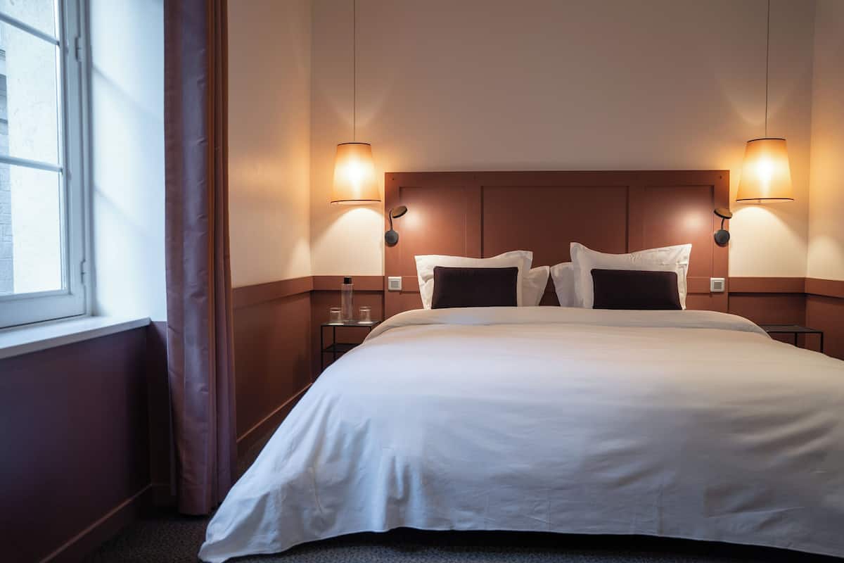 A hotel room with a large bed, two bedside tables, and two wall-mounted lamps.