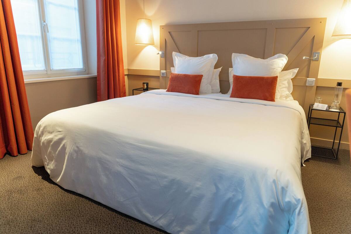 A hotel room with a large bed, two bedside lamps, a nightstand, and a window with curtains.