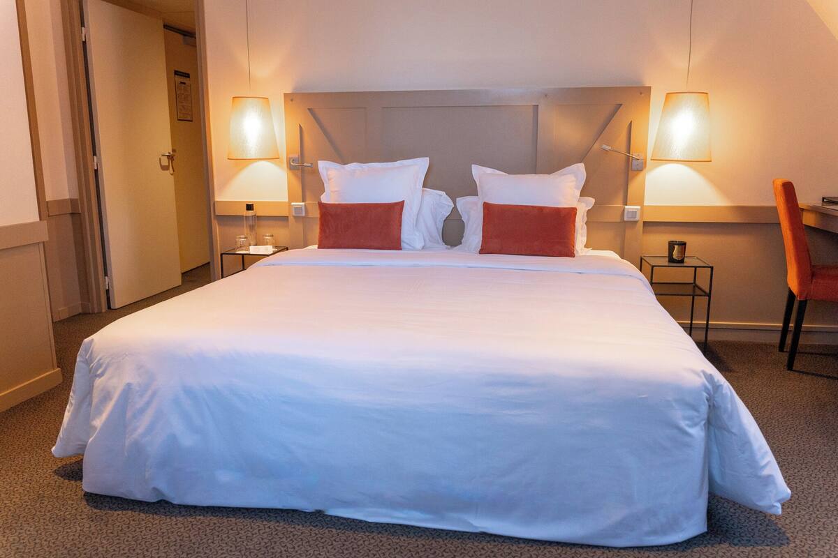 A large bed with white bedding and two red pillows, flanked by two bedside lamps.