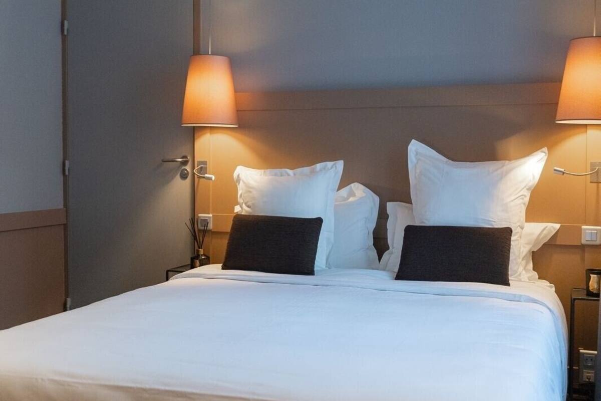 A neatly made bed with white and dark pillows, two bedside lamps, and a door to the left.