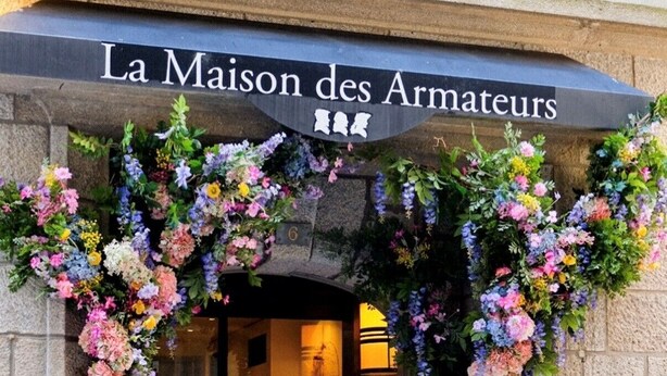 A hotel entrance with a sign reading 'La Maison des Armateurs' and a large floral archway.
