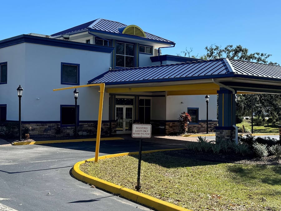 A modern building with a covered entrance, a sign indicating it is for registered guests only, and a parking area with yellow curbs.