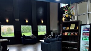 A modern lounge area with a sofa, a vending machine, and a view of a garden through large windows. - Days Inn by Wyndham Brooksville/Dade City (Brooksville)