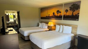 A hotel room with two beds, a desk, a mirror, and a painting of a sunset. - Days Inn by Wyndham Brooksville/Dade City (Brooksville)