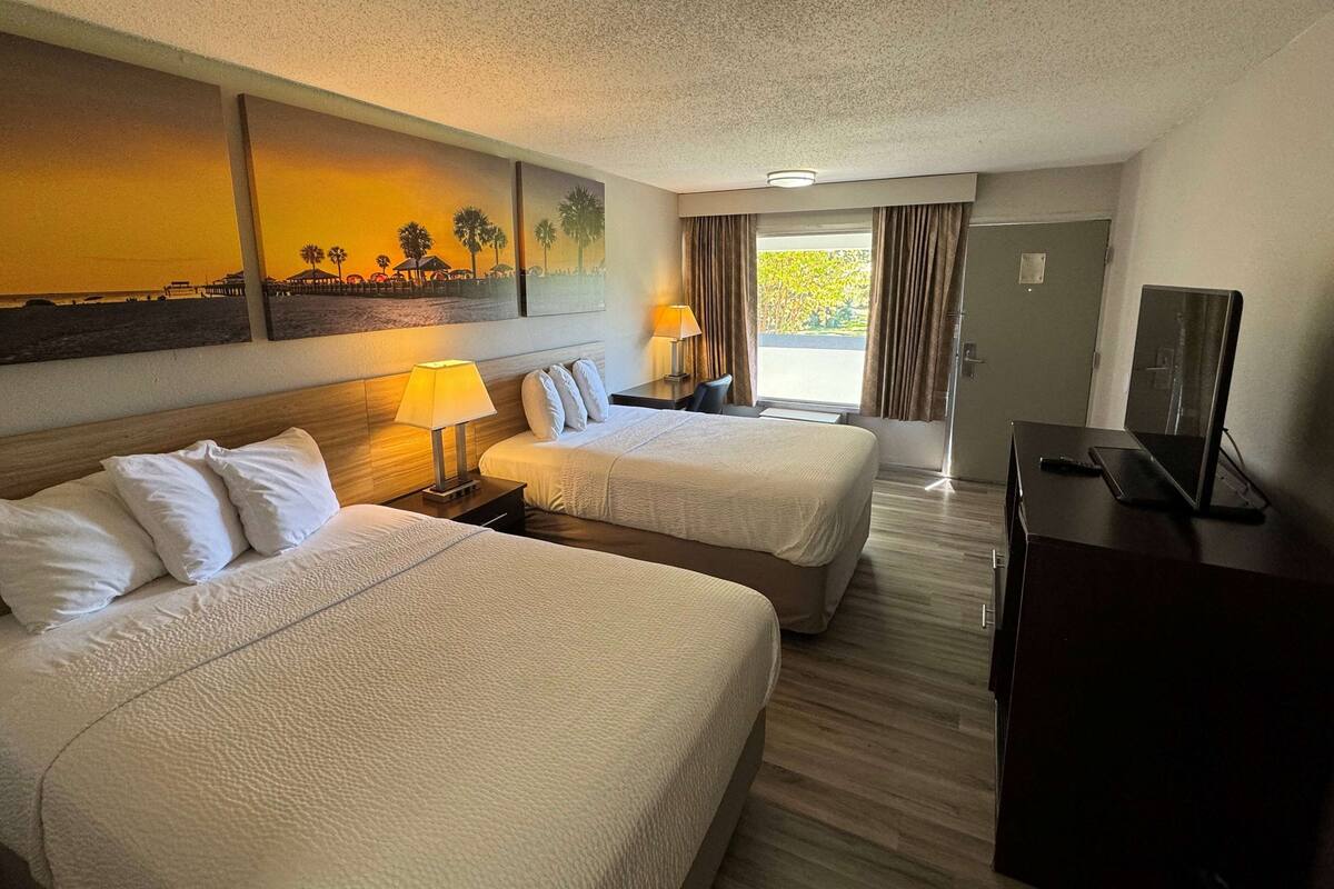 A hotel room with two beds, a desk, a TV, and a painting on the wall.