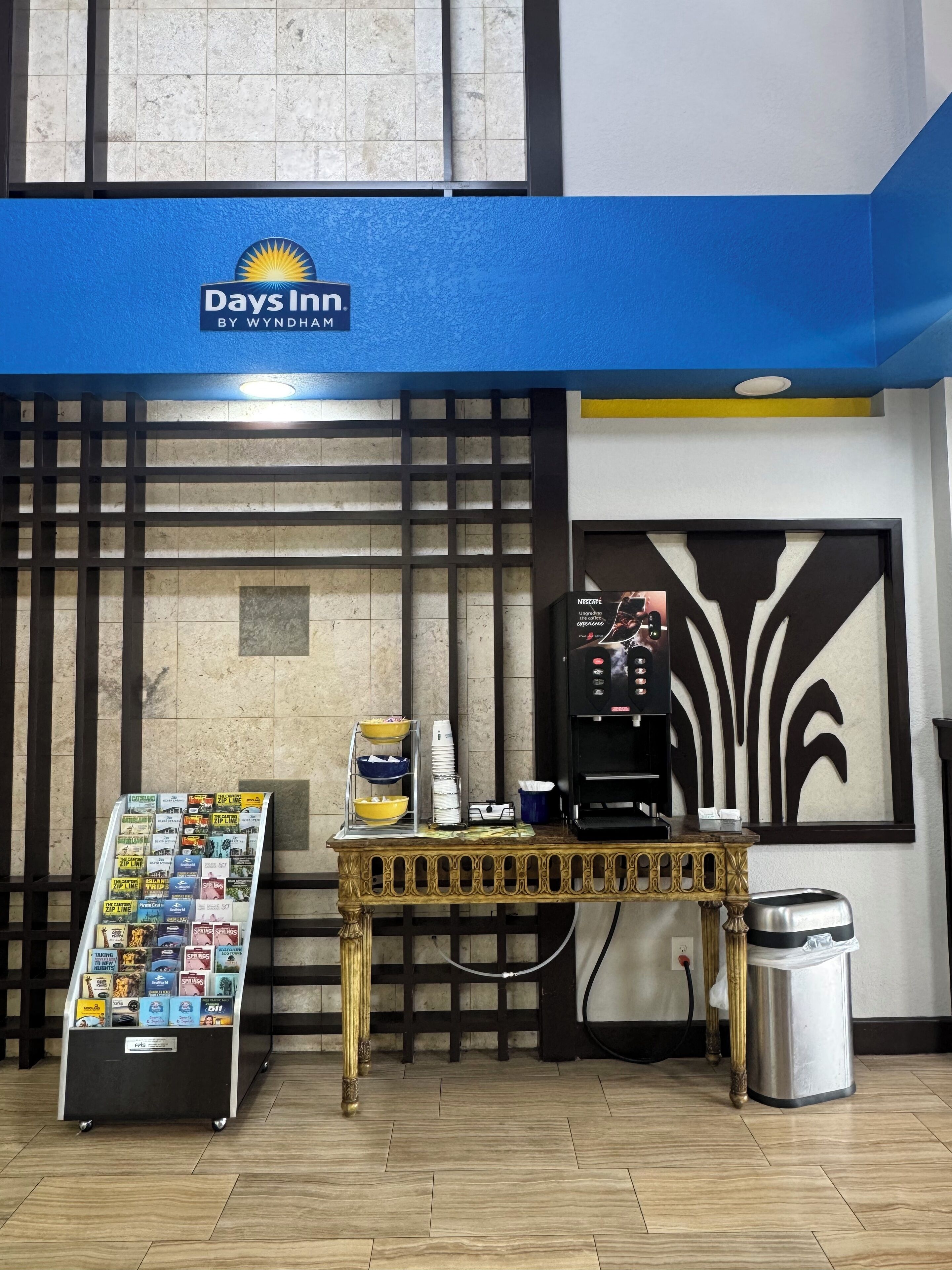 Área de recepção do Days Inn, com uma máquina de café, suporte para revistas e uma lixeira.