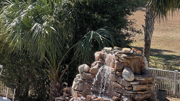 A pool with a stone waterfall feature, surrounded by rocks and palm trees. - Days Inn by Wyndham Brooksville/Dade City (Brooksville)