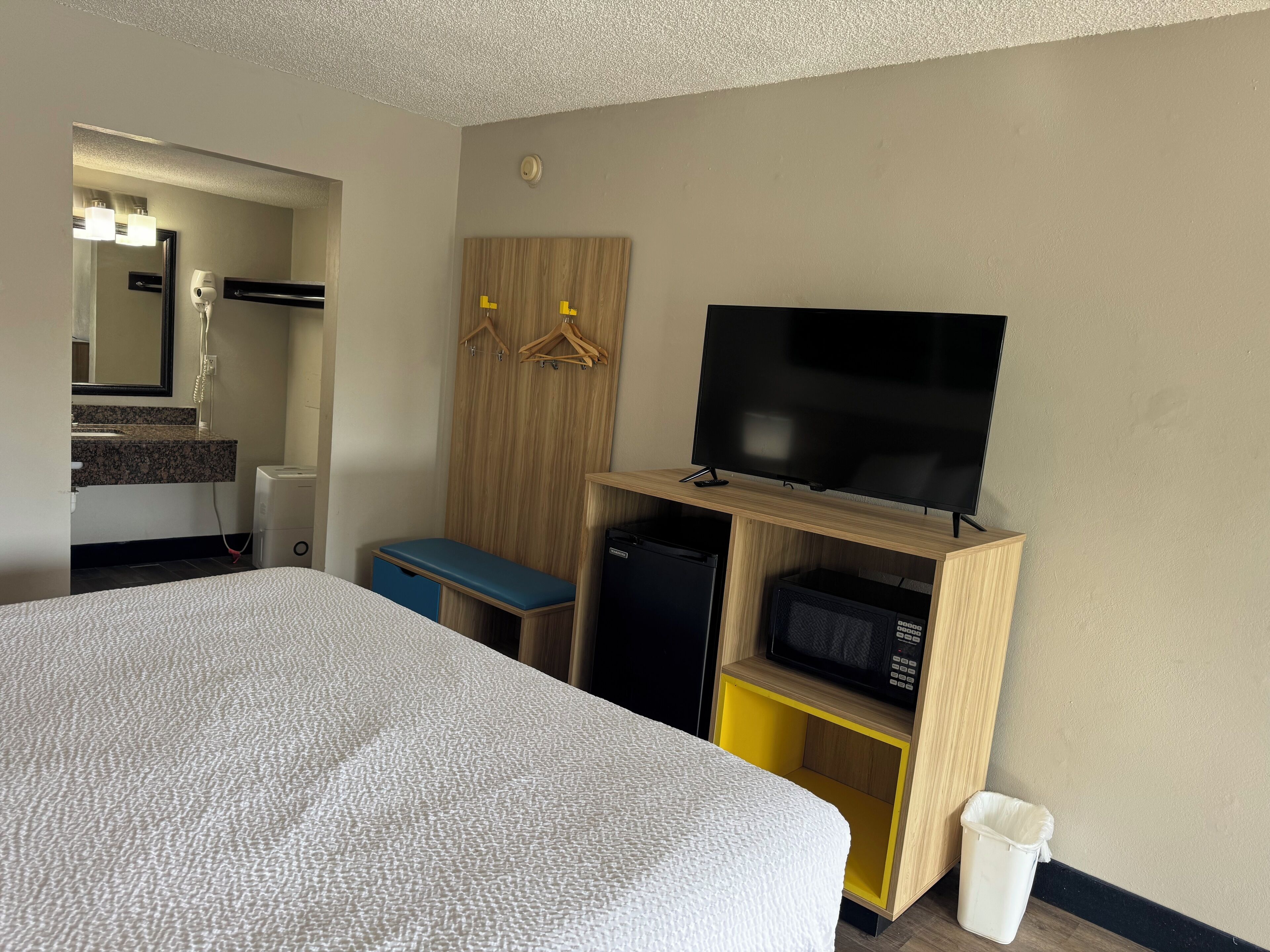 Et hotelværelse med seng, fjernsyn på træstel, mikroovn og en lille bænk.