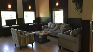 A spacious living room with a sofa, armchair, and a coffee table. There are two windows providing natural light and a view of greenery outside. - Days Inn by Wyndham Brooksville/Dade City (Brooksville)