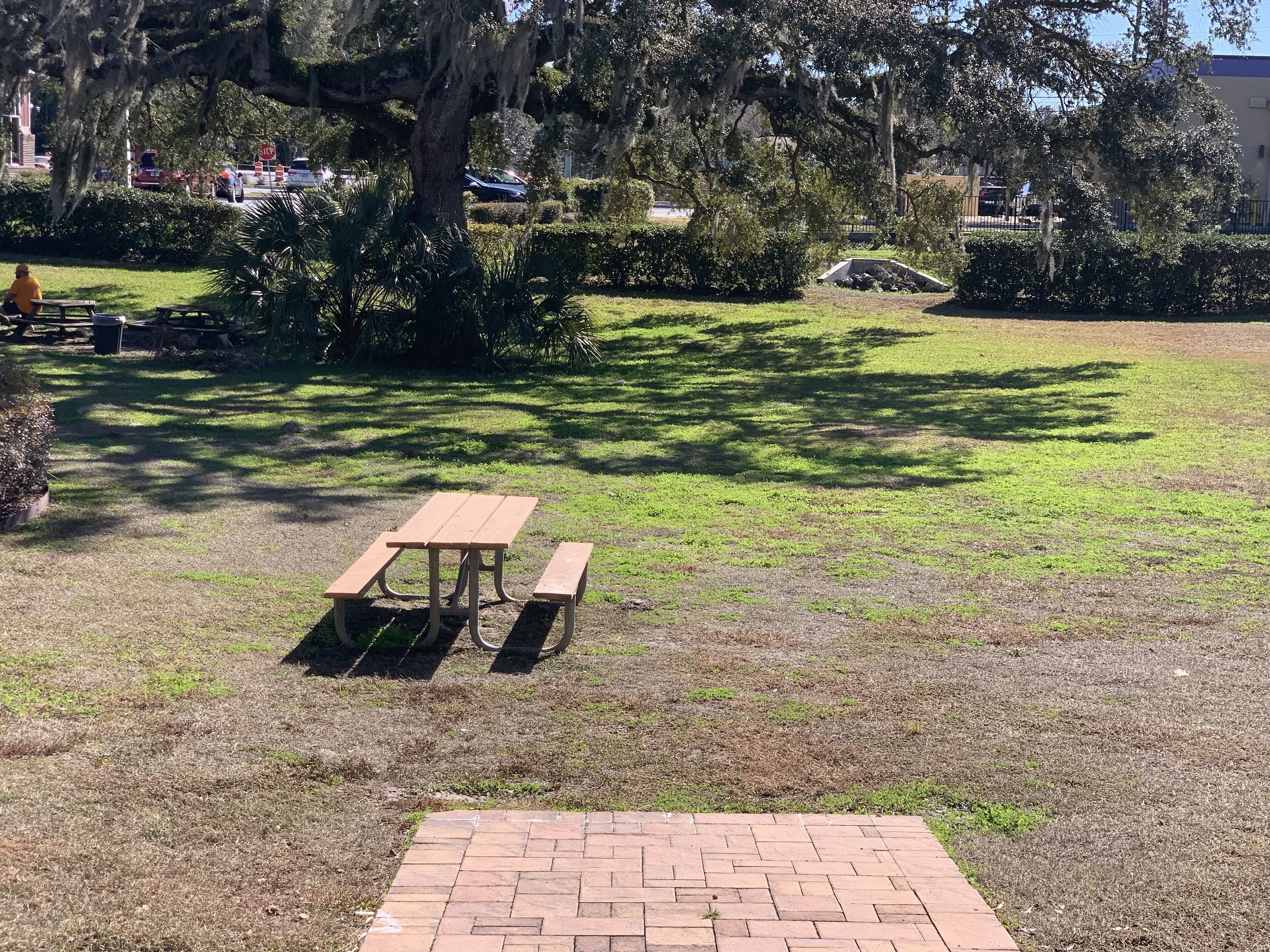 Una mesa de picnic y un banco en un área cubierta de césped, con árboles y un camino de ladrillo.