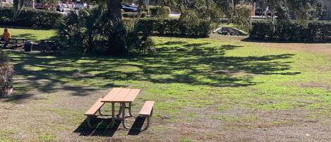 Una mesa de picnic y un banco en un área cubierta de césped, con árboles y un camino de ladrillo.
