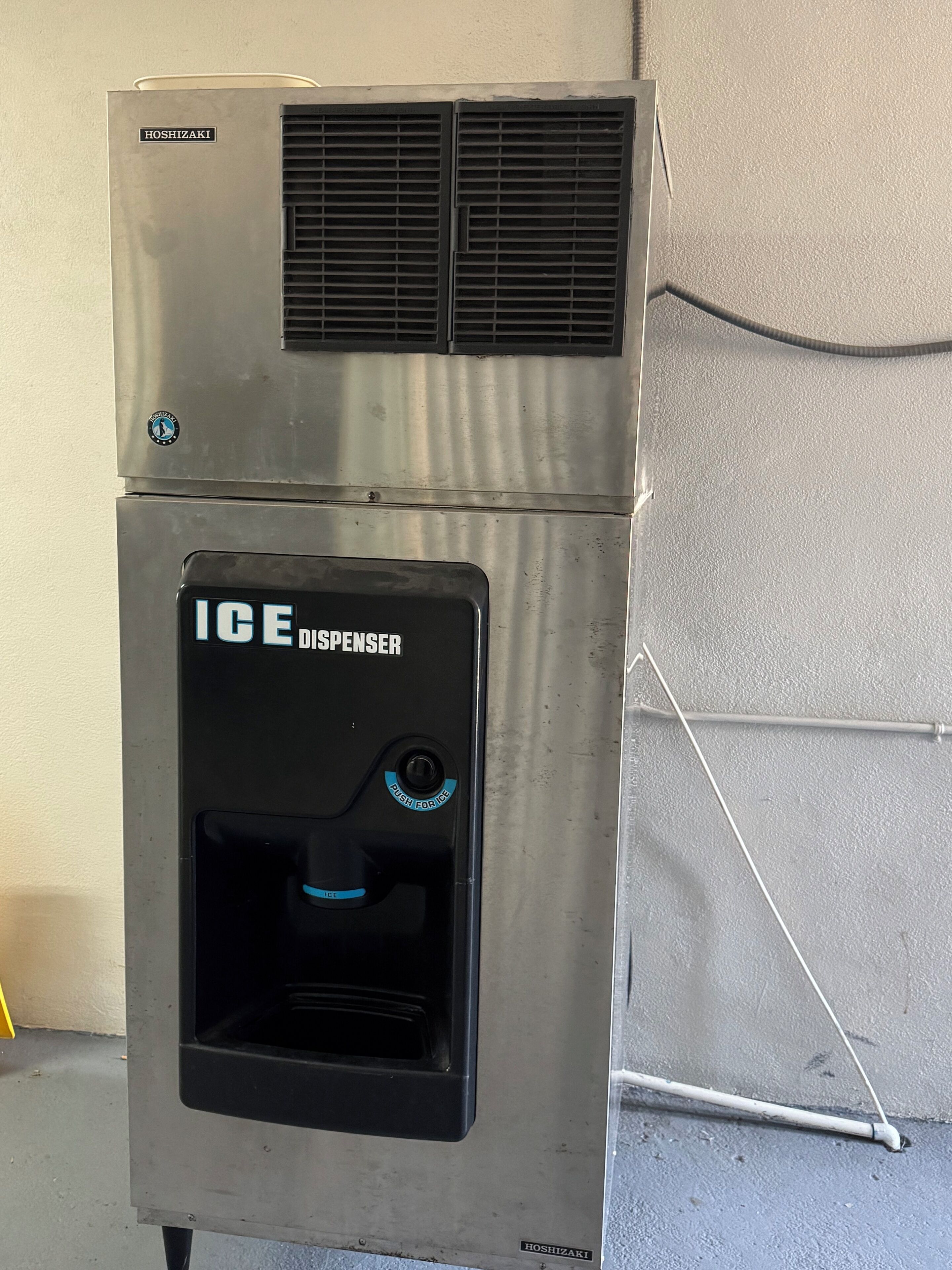 Dispensador de hielo de acero inoxidable con frente negro y un botón azul.