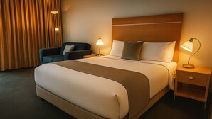 A hotel room with a large bed, two bedside tables, a chair, and a curtain.