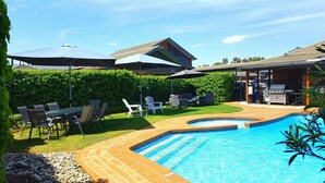 A backyard with a swimming pool, outdoor seating, and a barbecue area.