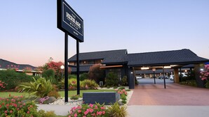 A hotel entrance with a sign reading "The Hernage MOTSA," featuring a covered parking area and landscaped gardens.