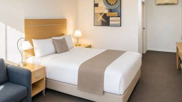 Una habitación de hotel con cama, mesitas de noche, lámpara, silla y una obra de arte en la pared.