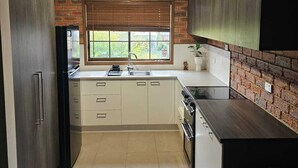 A modern kitchen with white cabinets, a brick accent wall, a window with blinds, and a stainless steel refrigerator.